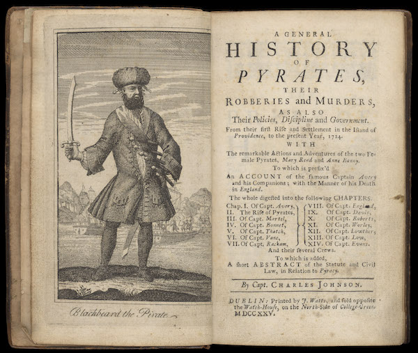 A photograph of a book open at the title page. The rich hand side says 'A General History of Pirates' with text underneath. On the left is a print of a pirate, he wears a frock coat with wide sleeves, a bandolier across his chest (a cross body belt) and holds a sword in his right hand. He wears a hat and has a big black beard. Underneath the illustration are the words 'Blackbeard the pirate'. 