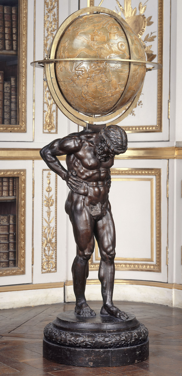 Photograph featuring a bronze statue of a person holding a globe, resembling the figure of Atlas. This sculpture is displayed indoors in a museum setting. The man's head is bent slightly down and the globe rests upon his shoulders.