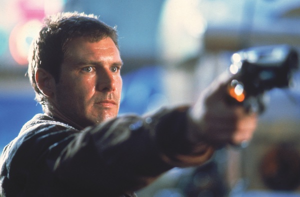 A film still from Blade Runner showing the actor Harrison Ford. He is a white man with short brown hair, his head and shoulders are show in his right hand he hold a gun with hand arm raised parallel to shoulder height.
