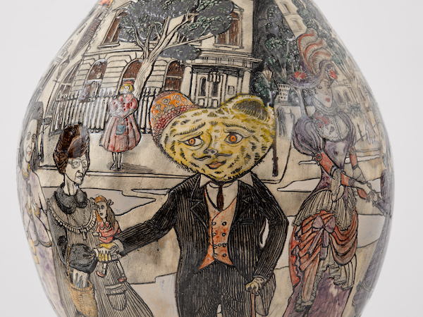 A close up photograph of a ceramic vessel. It has a flat illustrated design covering the surface. It shows Grayson Perry's teddy bear Alan Measles dressed in a black suit and waistcoat. It also features an illustrated version of the artist Grayson Perry's alter ego 'Claire'. There are other female figures set in a street scene with grand buildings behind and trees on the pavement behind the characters. 